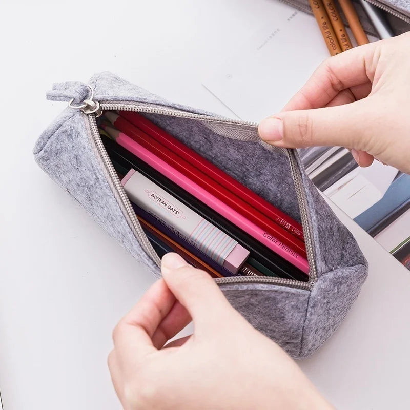 Gray pencil case with stationery items on a white surface