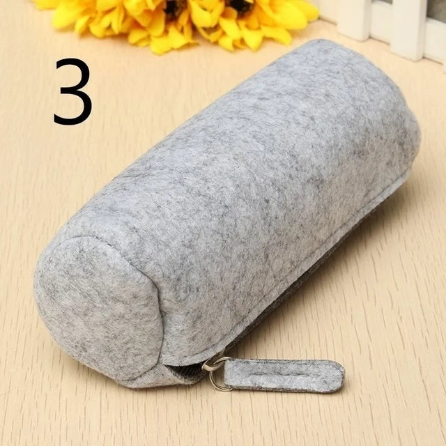 Gray cylindrical pillow with a keychain on a beige surface with yellow flowers in the background.