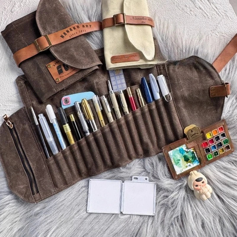 Roll-up art supply organizer with pens, watercolors, and notepads on a textured surface