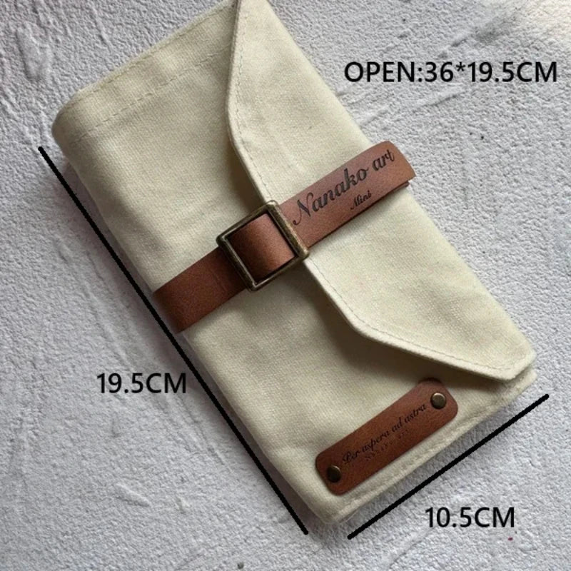 Beige canvas pencil case with brown leather straps and measurements on a gray background