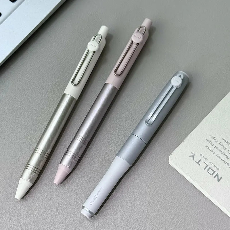 Three pens of different colors on a gray surface with a card in the corner.
