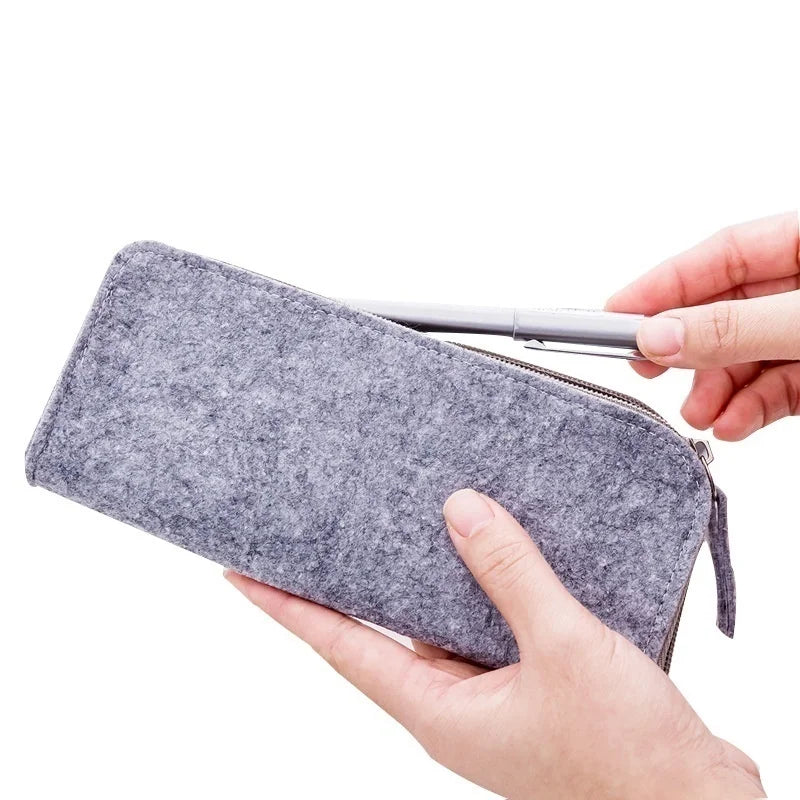 Person holding a gray felt pencil case with a pen on a white background