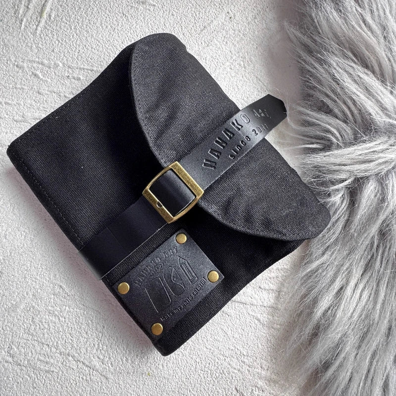 Black canvas pencil case with leather belt with gold buckle on a textured white surface