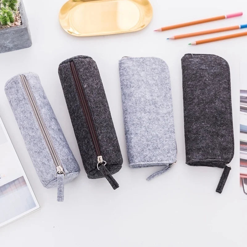 Four gray felt pencil cases with zippers on a white surface.