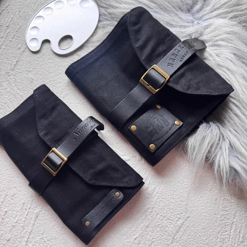 Two black leather pencil cases with gold buckles on a textured surface.