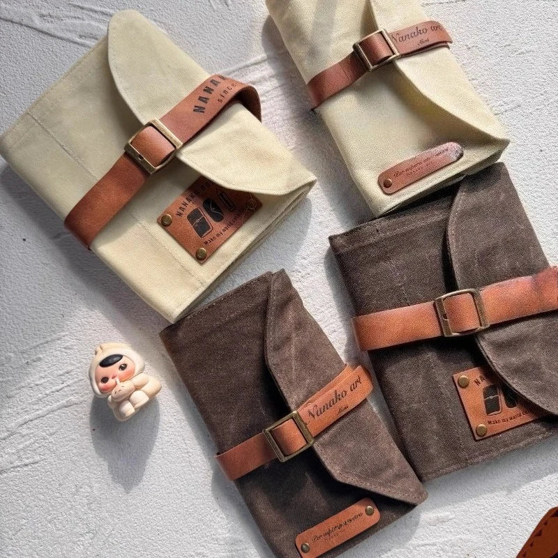 Three fabric pencil cases with leather straps on a textured surface